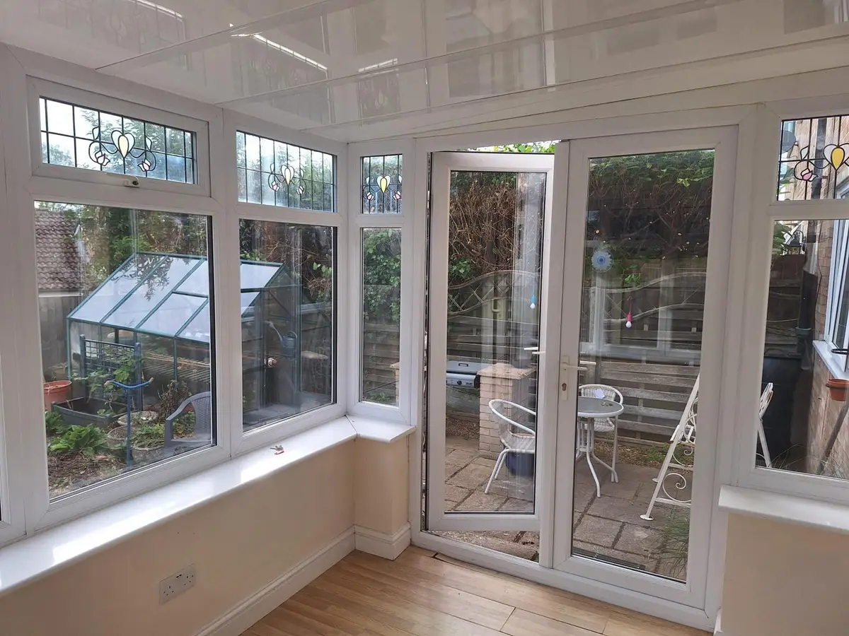Bright conservatory with a glossy white panel ceiling and French doors to the patio