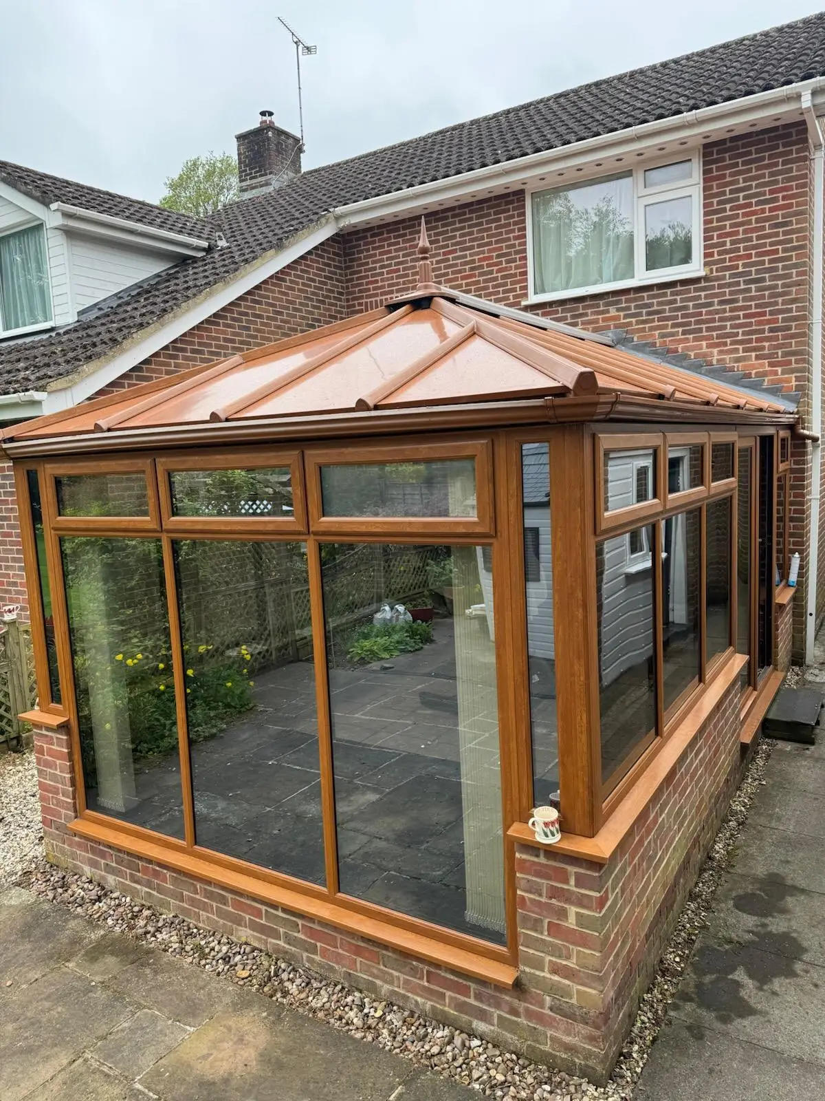 Side view of an oak-effect conservatory finished with a copper-coloured panel roof