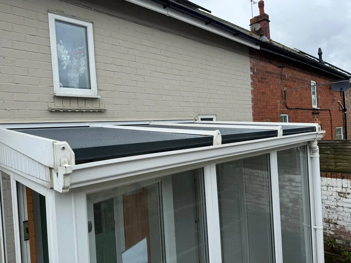 Lean-to conservatory with new dark grey insulated roof panels on white glazing bars