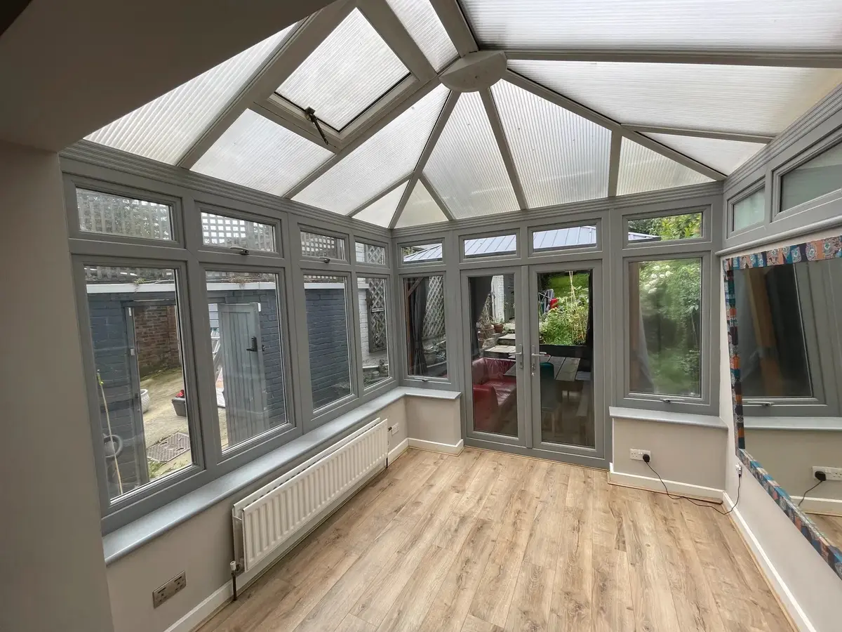 Inside a grey-framed conservatory with an old polycarbonate roof and roof vents, before replacement