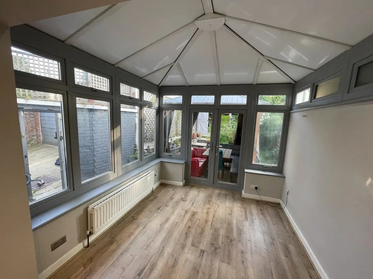 Grey-framed conservatory with a bright white insulated panel ceiling and oak-effect flooring