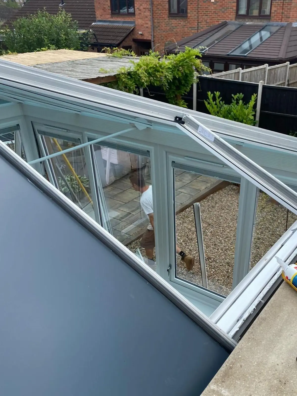 Grey insulated roof panel being sealed at the eaves, with a sealant gun on the wall top