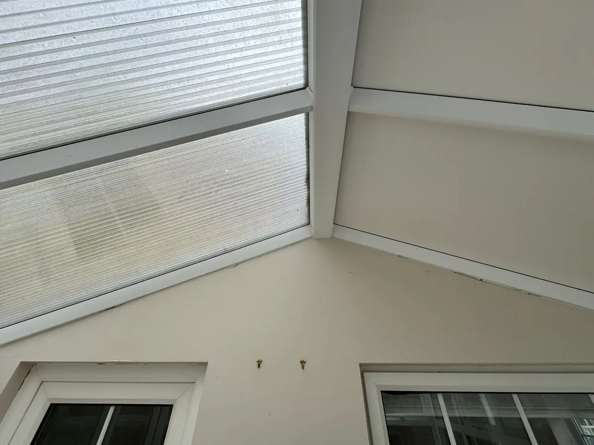 Inside a conservatory mid-installation, with old polycarbonate on one slope and new white panels on the next