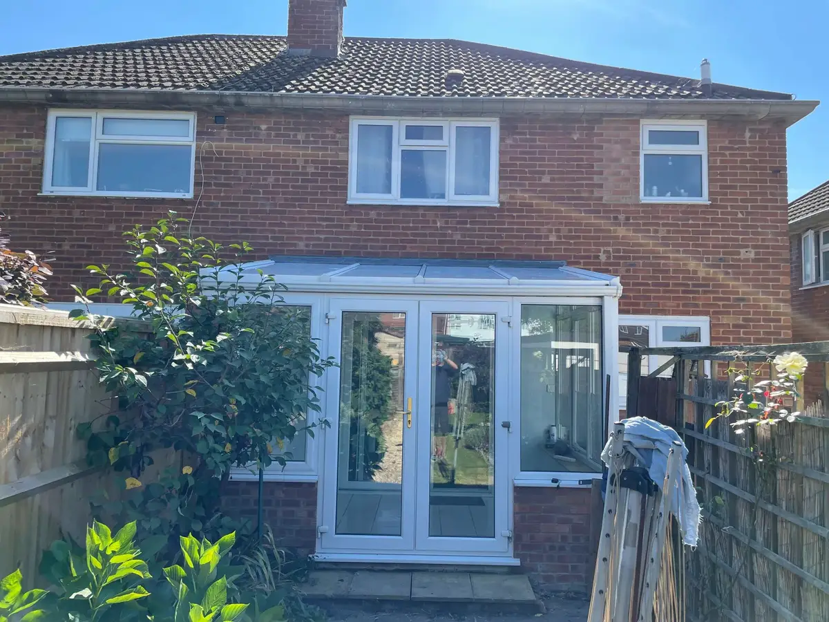 Rear of a red brick semi with a finished white panel roof on the lean-to conservatory