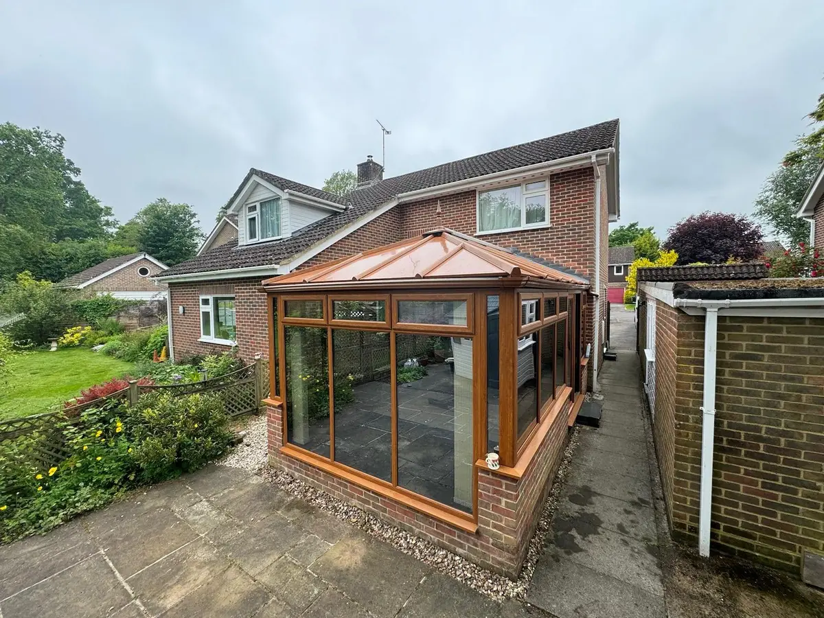 Oak-effect conservatory with a new copper-coloured insulated panel roof beside a garden