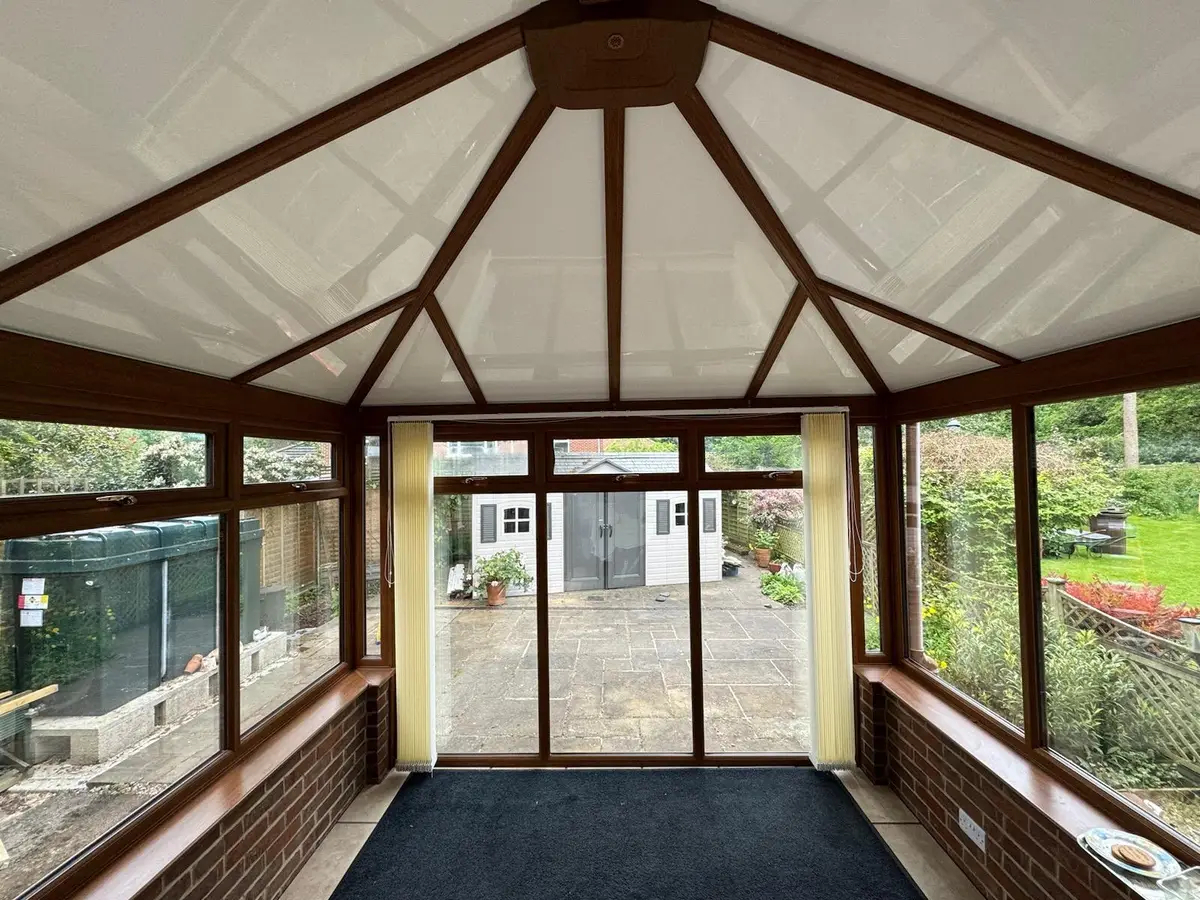 Oak-effect rafters framing a white insulated panel ceiling inside a conservatory