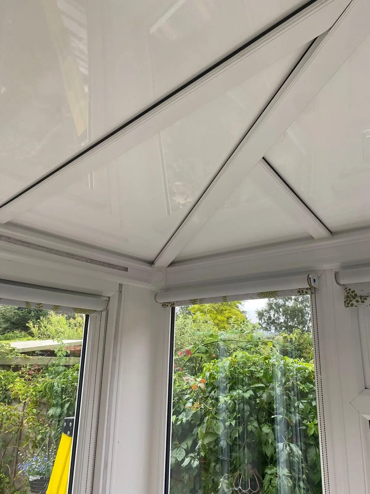 Corner of a conservatory with a white insulated panel ceiling above the garden windows