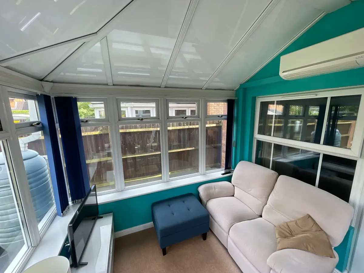 Conservatory lounge with a cream sofa and air conditioning unit under a white panel roof