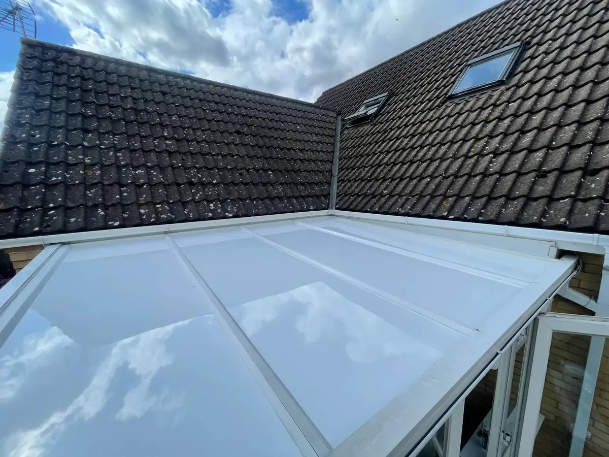 New white conservatory roof panels reflecting the clouds, set against a dark bungalow roof