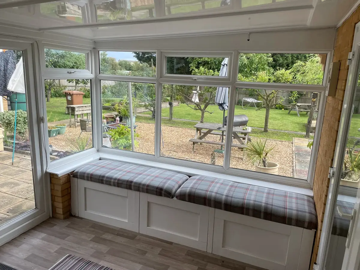 Window seat with checked cushions under a white panel roof, looking out over a large garden