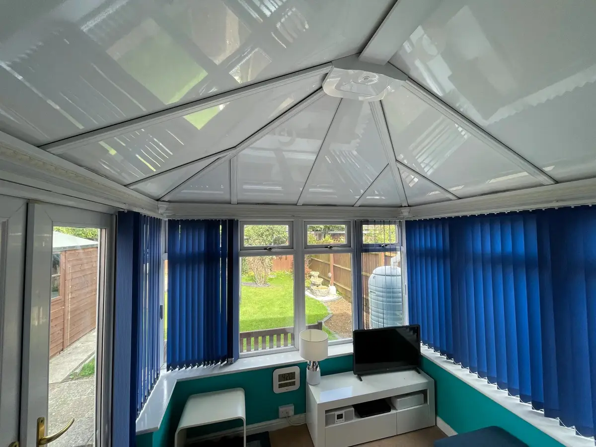 Teal-walled conservatory with blue blinds under a new white insulated panel ceiling