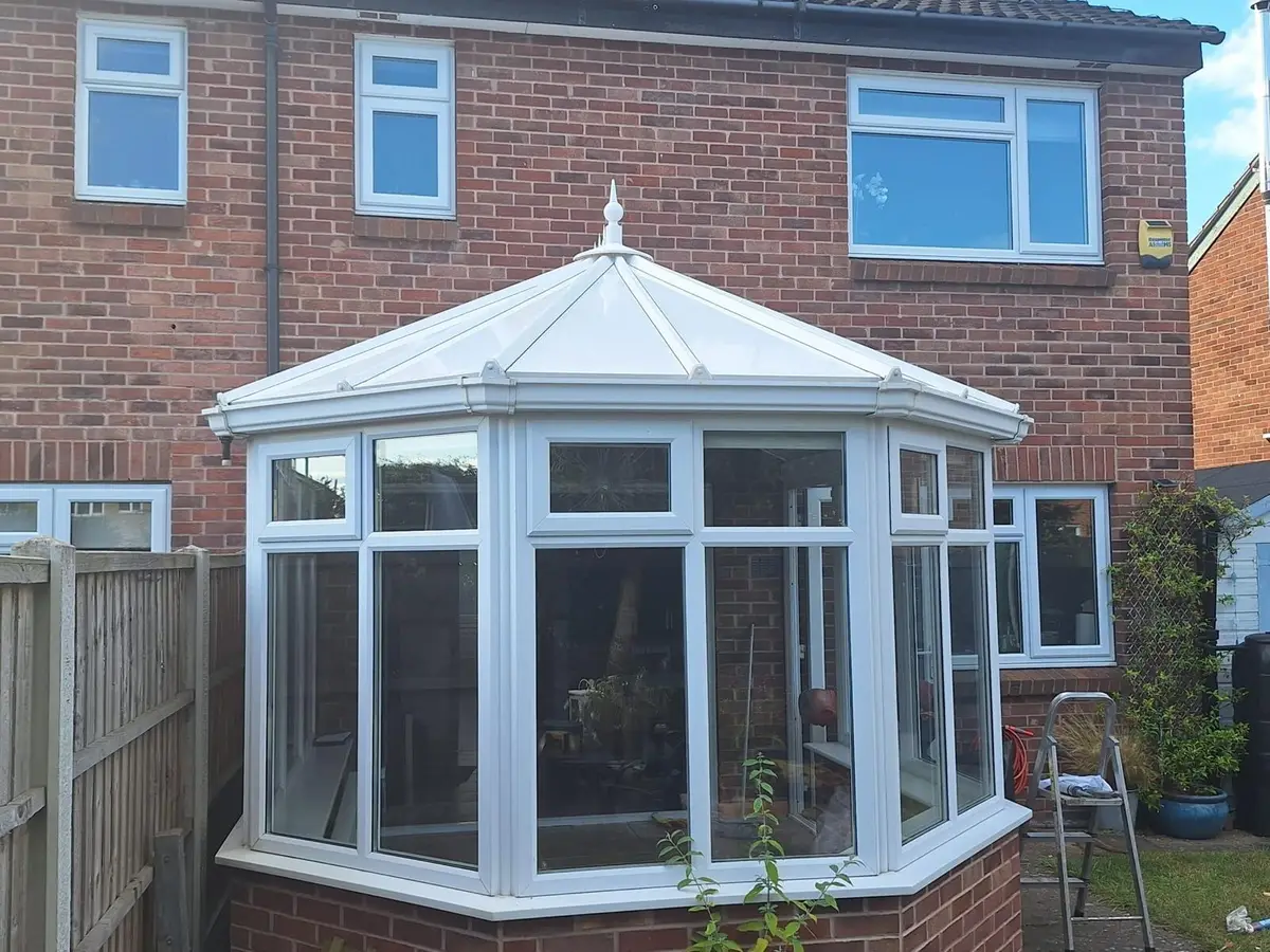Full view of a Victorian conservatory with a new white insulated panel roof behind a brick house