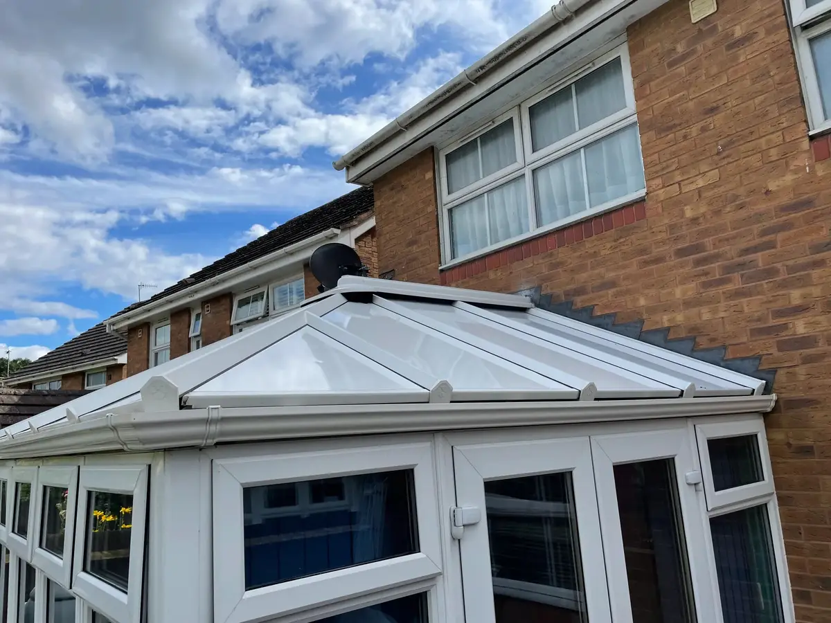 Smooth white insulated panel roof with capped glazing bars under a bright blue sky