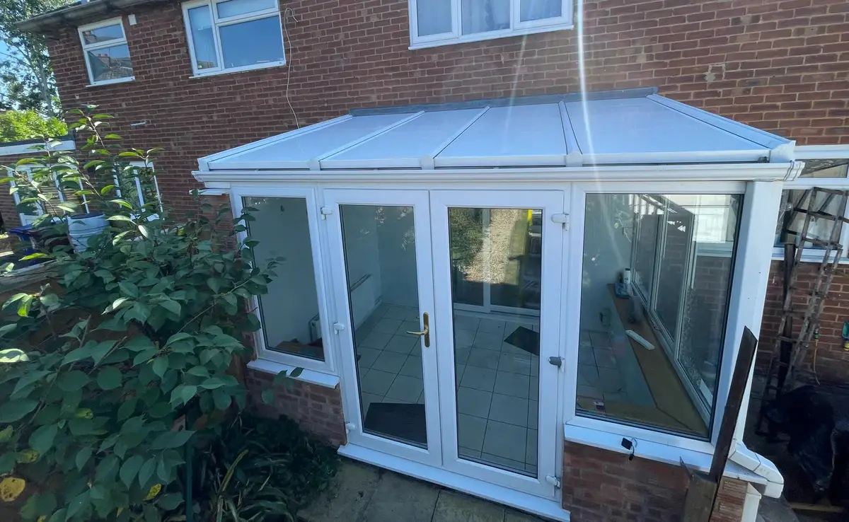 Lean-to conservatory with a new white insulated panel roof in afternoon sunshine