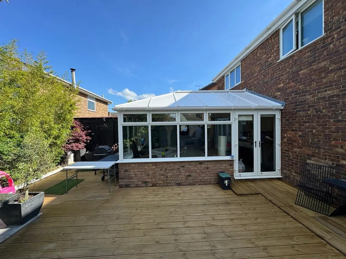 White conservatory with a finished insulated panel roof overlooking a timber deck
